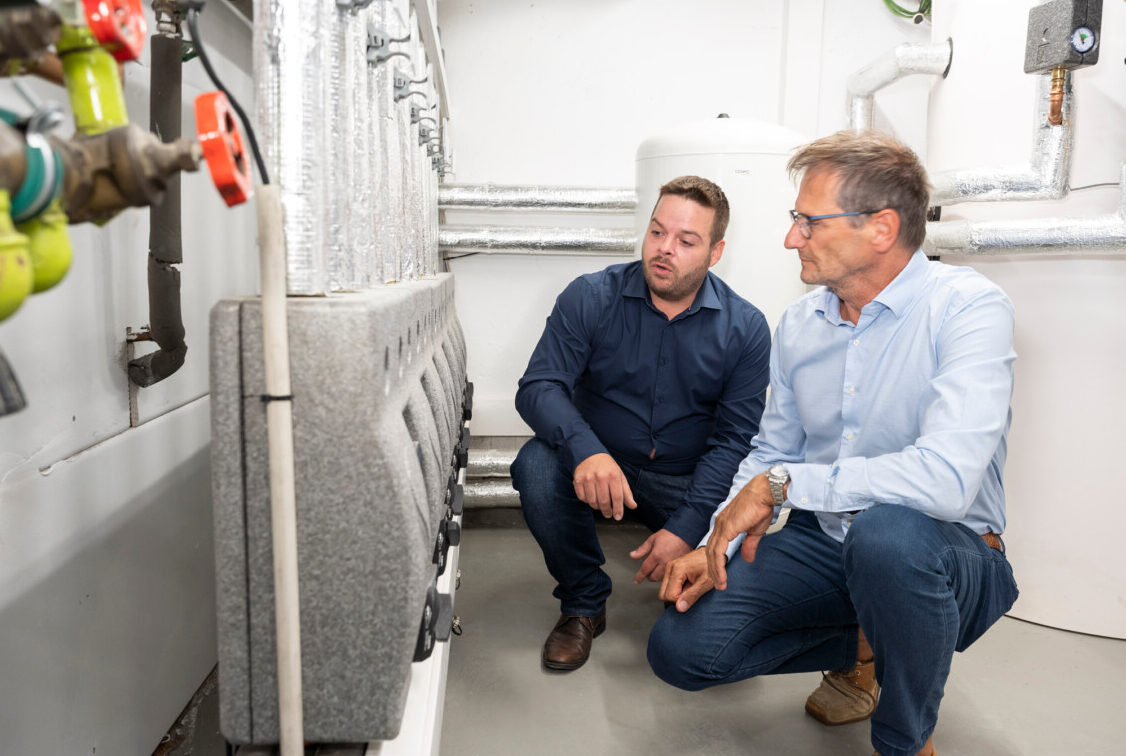 Foto zeigt zwei Personen vor einer Heizungsanlage.