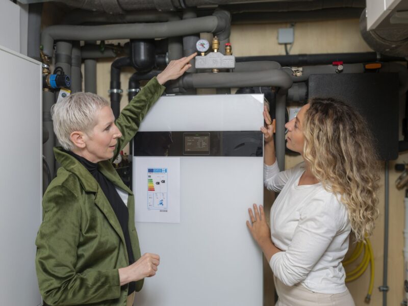 Junge Frau mit Energieberaterin vor Wärmepumpe-Foto Zukunft Altbau