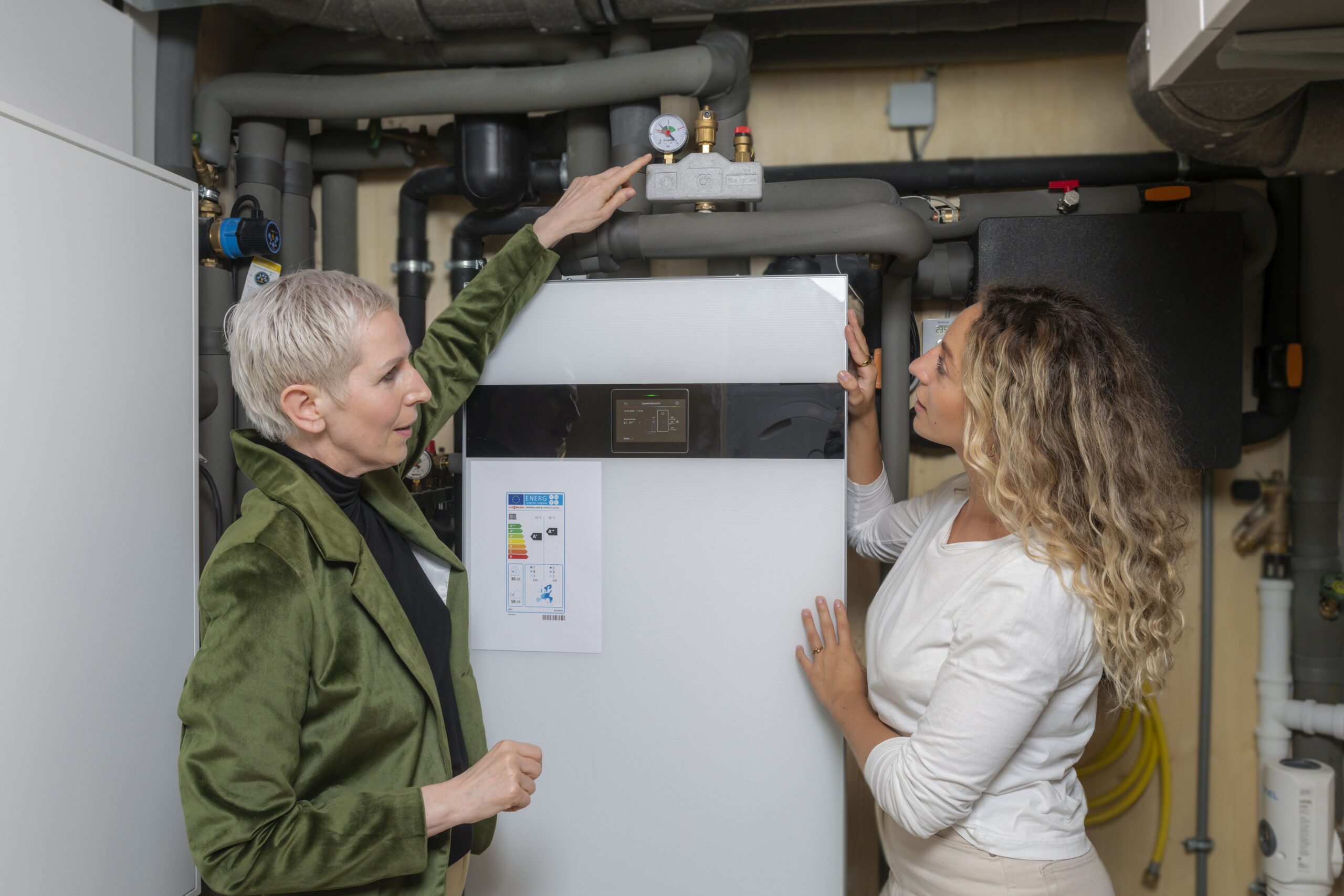 Junge Frau mit Energieberaterin vor Wärmepumpe-Foto Zukunft Altbau